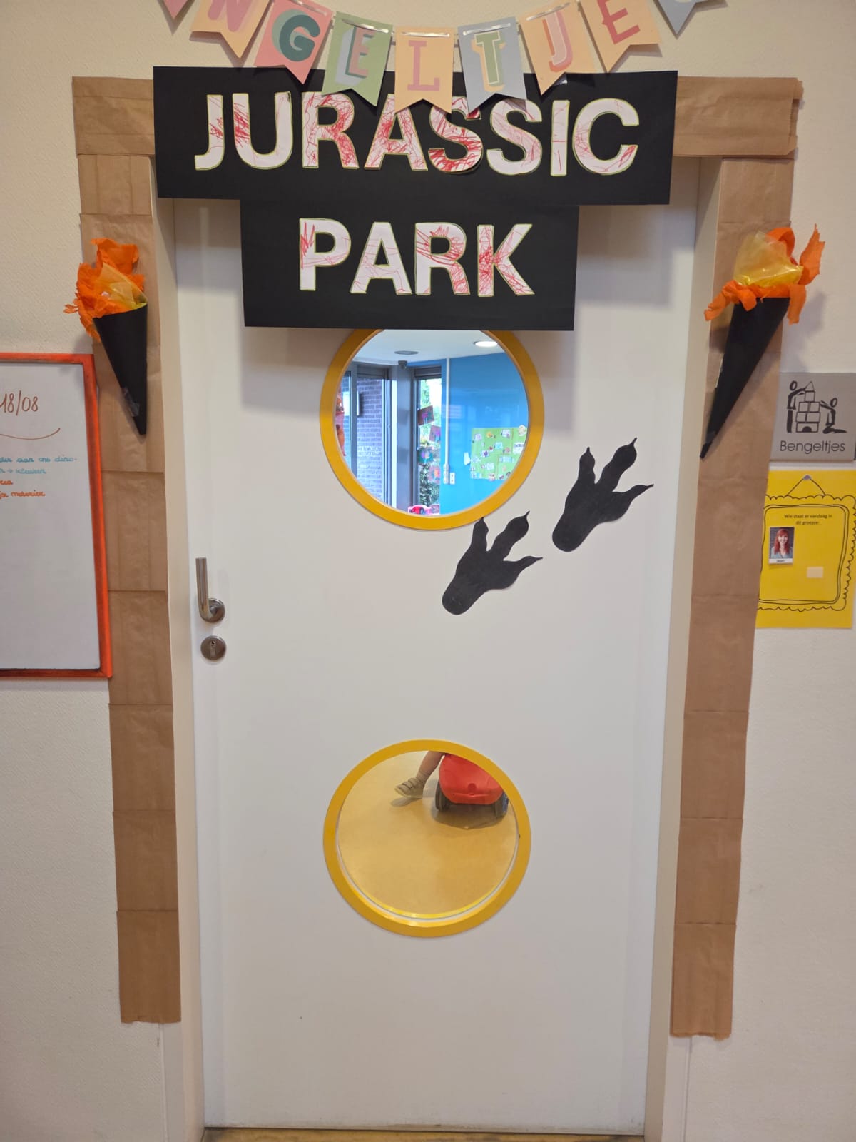 De witte deur is versierd met een "Jurassic Park" bord, twee zwarte dinosaurusvoeten en twee papieren fakkels.